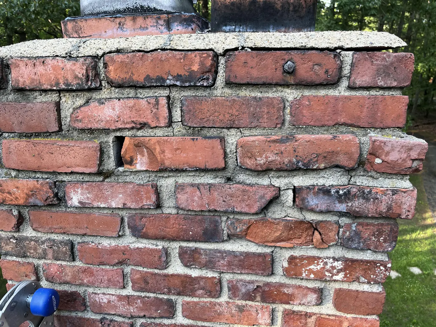 Eroded mortar joints and cracked bricks near the top of an older brick chimney